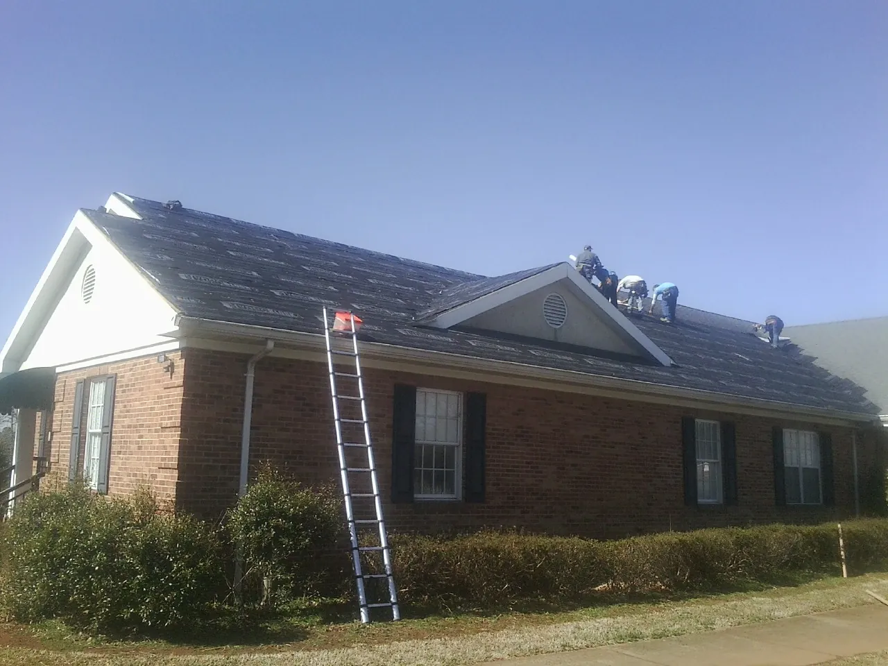 Crew tearing shingles off a brick ranch roof with a ladder set — Metal Roof Repair work by our crew in Coshocton