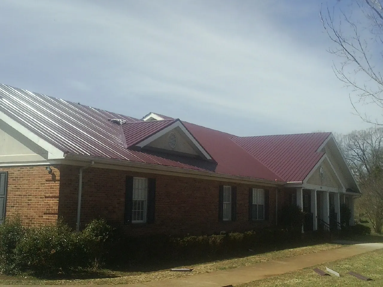 Red metal roof with gabled entries on a long brick building, from a Hail Damage Roof Repair job in Coshocton