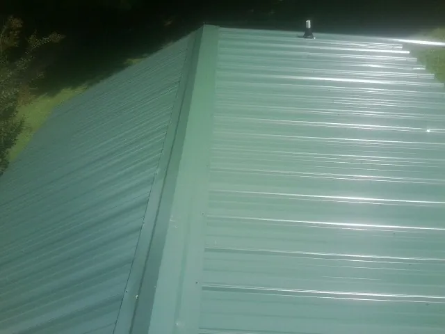 New green metal panels meeting at the ridge of a roof — Flat Roof Repair work by our crew in Coshocton