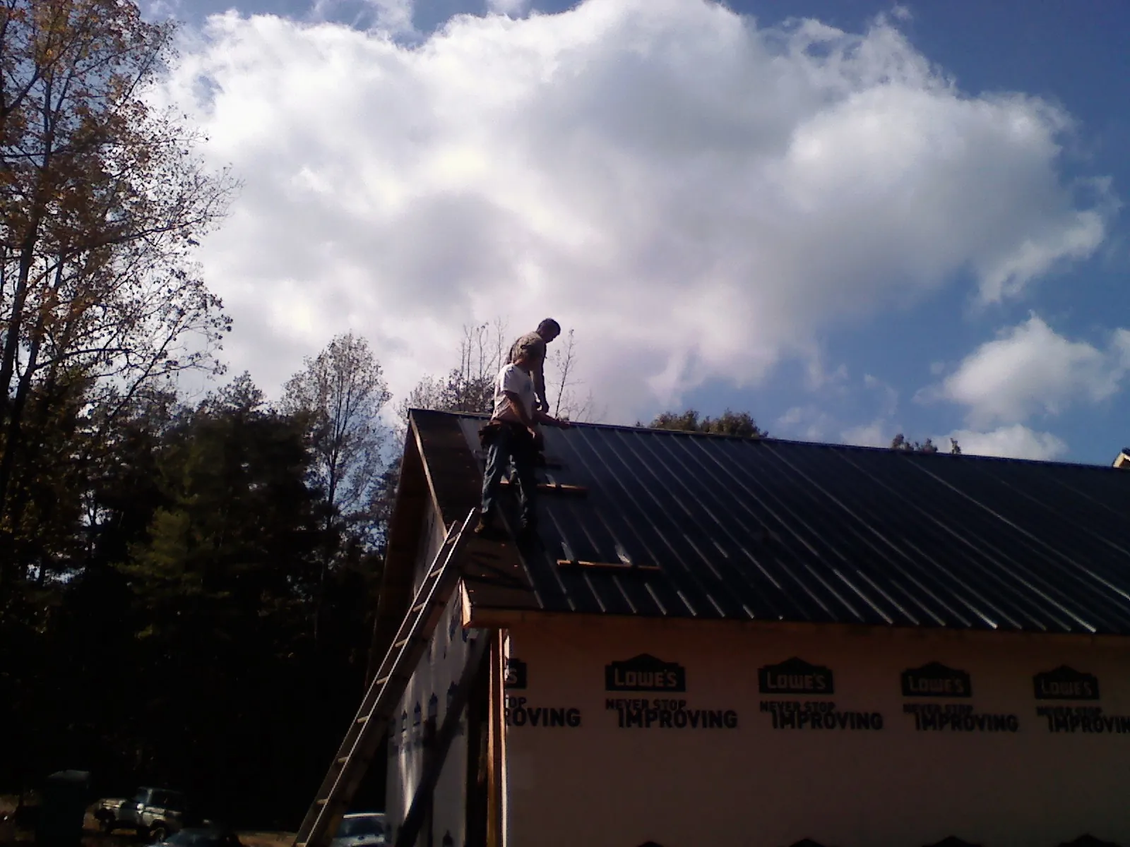 Roofer fastening dark metal panels high against a cloudy sky, from a Roof Inspection job in Coshocton