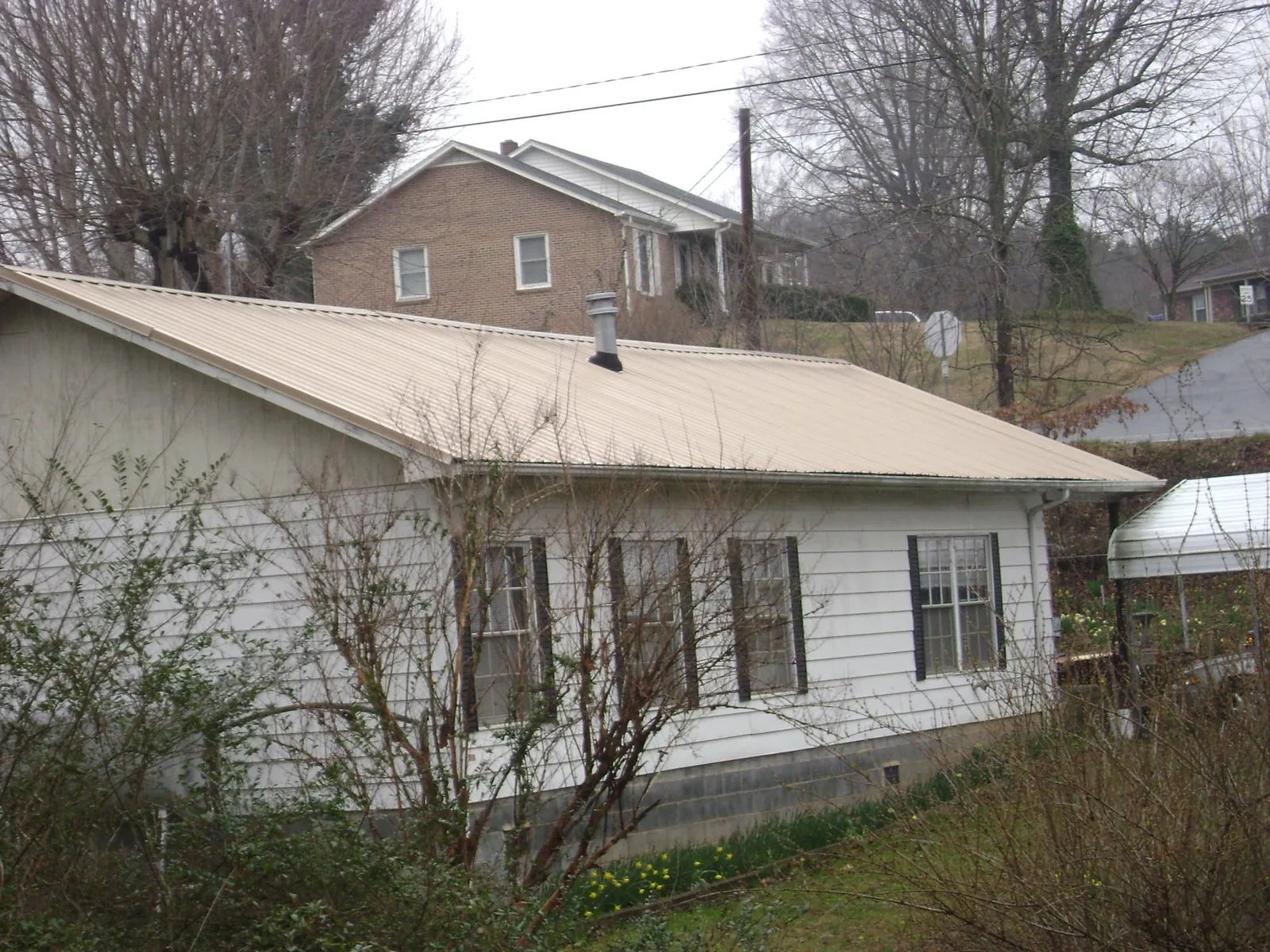 Tan metal roof on a white sided house set into a hillside — Commercial Roofing by Roofing Brothers in Coshocton