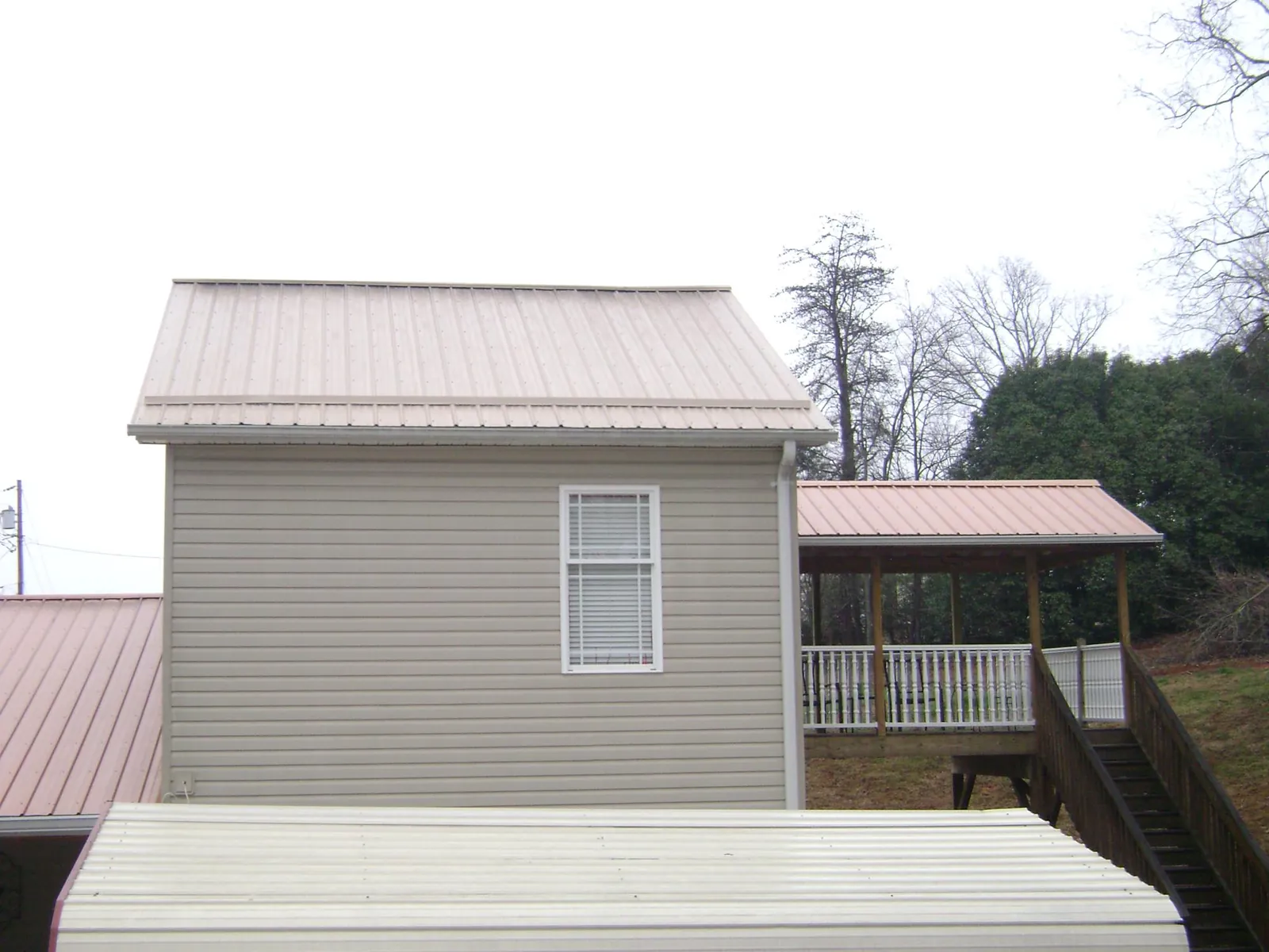 Tan metal roofs on a two story addition and attached porch, from a Roof Replacement job in Coshocton