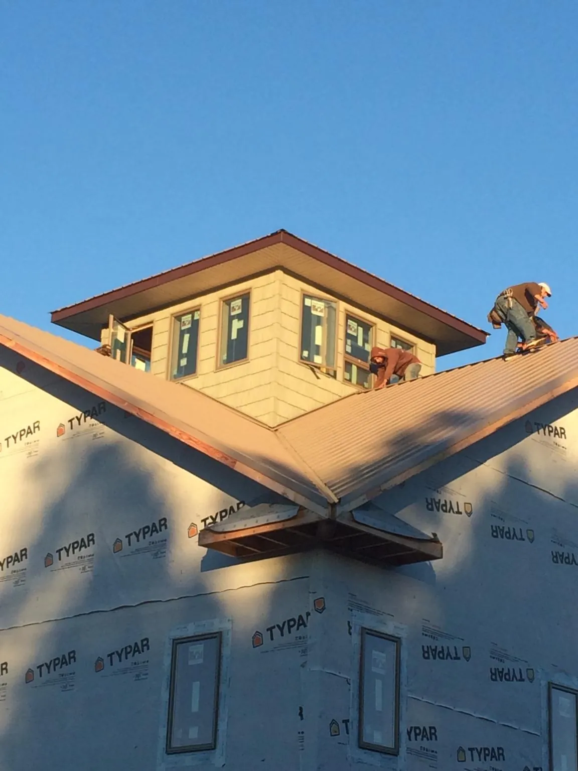 Roofers working around a rooftop cupola on a new metal roof at sunset — Roof Waterproofing in Coshocton by Roofing Brothers